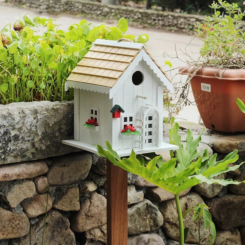 "Natural Wood House" wooden birdhouse on garden stake displayed on stone wall border surrounded by lush green plants and terracotta pots, outdoor garden setting