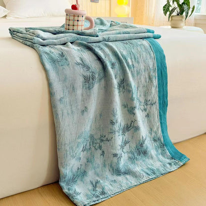 Teal Garden bamboo fibre jacquard blanket draped over a white bed frame, featuring a botanical fern and grass pattern in teal tones with a solid teal border trim
