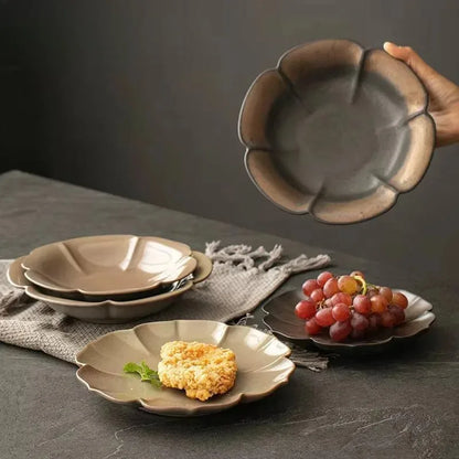 Three petal-shaped ceramic dishes in charcoal and ivory glaze holding grapes, dumplings and cherry tomatoes on a dark stone surface