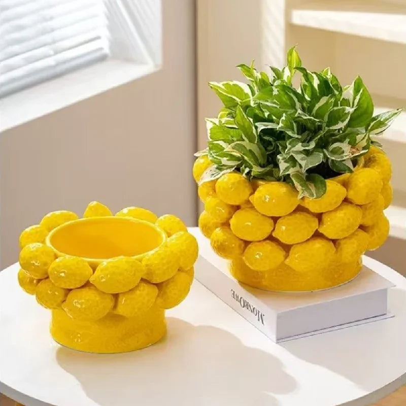 Two yellow ceramic lemon relief vases displayed together on a white round table, Small Bowl empty and Large Bowl styled with a green variegated plant, warm natural light, bright living room setting