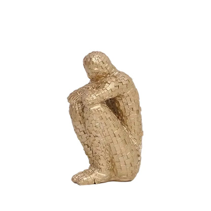 Yellow mosaic resin figure sculpture in a seated, contemplative pose on a white background.