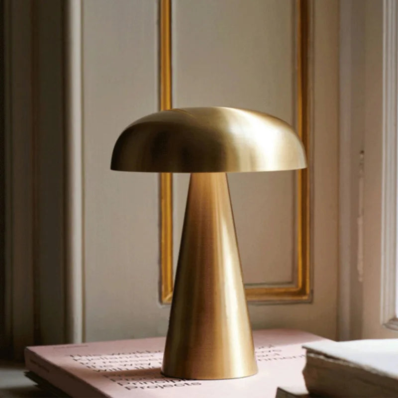 Cap & Glow mushroom table lamp in Golden finish placed on a stack of books against an elegant panelled wall, capturing a warm, sophisticated interior atmosphere.