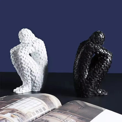 White and black mosaic resin figure sculptures standing on an open magazine against a dark blue background.