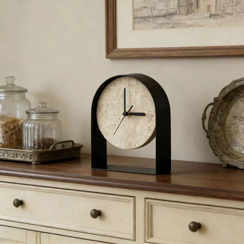 Black arched travertine table clock on a wooden sideboard beside glass storage jars and a vintage metal tray