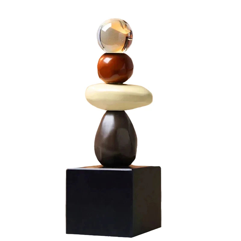 Abstract ceramic stacked sculpture with a clear upper sphere, brown rounded sphere, cream oval form, dark brown lower form and black square base, isolated against a white background.