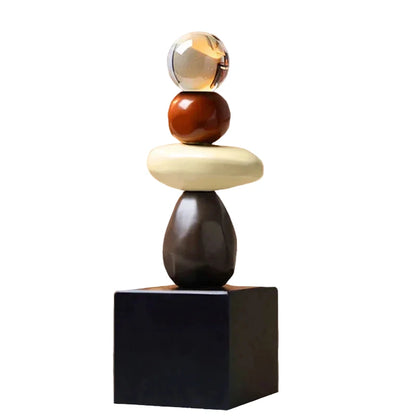 Abstract ceramic stacked sculpture with a clear upper sphere, brown rounded sphere, cream oval form, dark brown lower form and black square base, isolated against a white background.