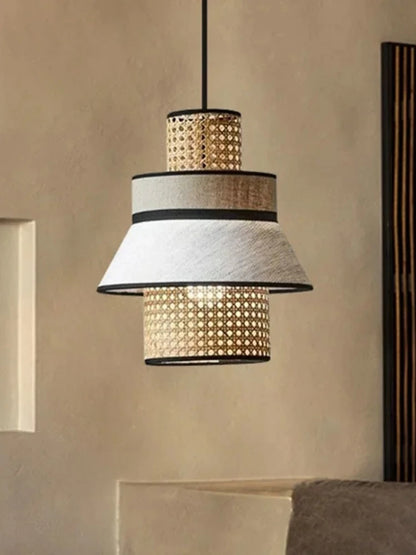 "Layer & Loom" tiered rattan and linen pendant light glowing warm amber, suspended against a textured neutral wall with japandi styling
