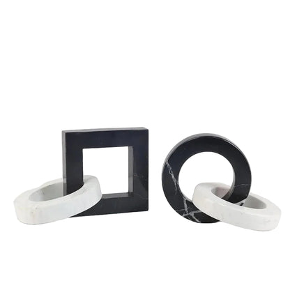 Round and square black and white interlocking marble sculptures styled together on a book and a neutral surface