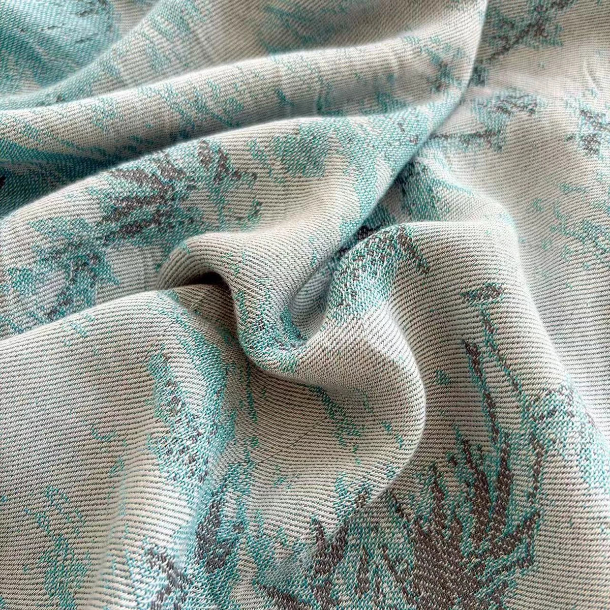 Close-up of the Teal Garden bamboo fibre jacquard blanket fabric showing the detailed botanical fern weave pattern in soft teal and sage tones with a smooth silky texture