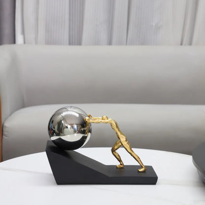 Silver Sphere version of The Ascent metal Sisyphus sculpture displayed on a white coffee table, with a cream sofa in the background.