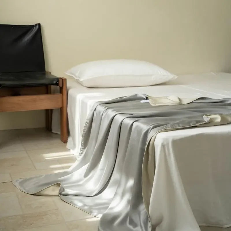 Pearl Silver 100% Tencel cooling summer blanket draped over a bed in a minimalist bedroom