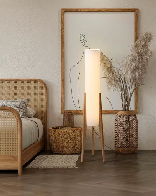  "Tripod & Cylinder" oak floor lamp glowing warmly beside a rattan bed, pampas grass and a line art print in a japandi bedroom