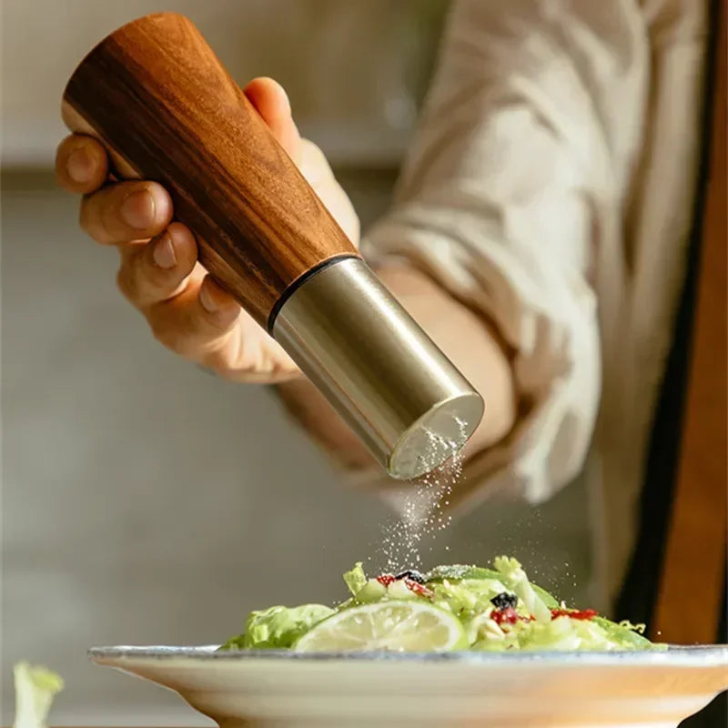 Acacia Twist pepper mill held in hand grinding fresh seasoning over a green salad on a ceramic plate
