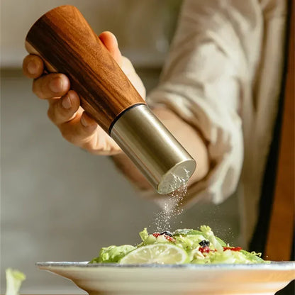 Acacia Twist pepper mill held in hand grinding fresh seasoning over a green salad on a ceramic plate