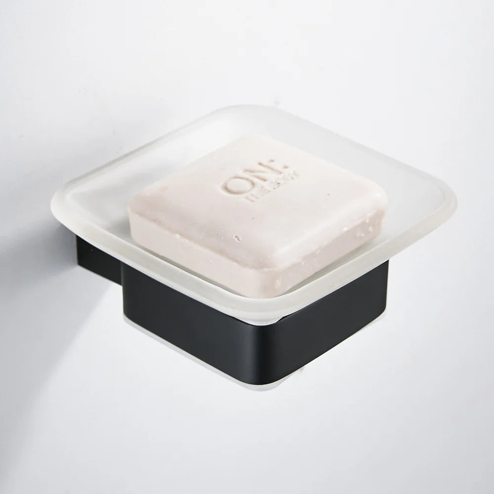 Wall-mounted matte black soap dish with frosted glass tray holding a white bar soap, mounted on white wall