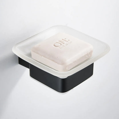 Wall-mounted matte black soap dish with frosted glass tray holding a white bar soap, mounted on white wall