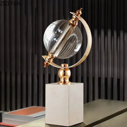 Crystal globe sculpture with gold-plated ring and white marble base, styled against dark ribbed wall panel on a desk surface