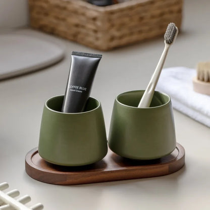 Two cone-shaped matte green ceramic cups on oval acacia wood tray, vintage green finish, bathroom toothbrush holder set, white background
