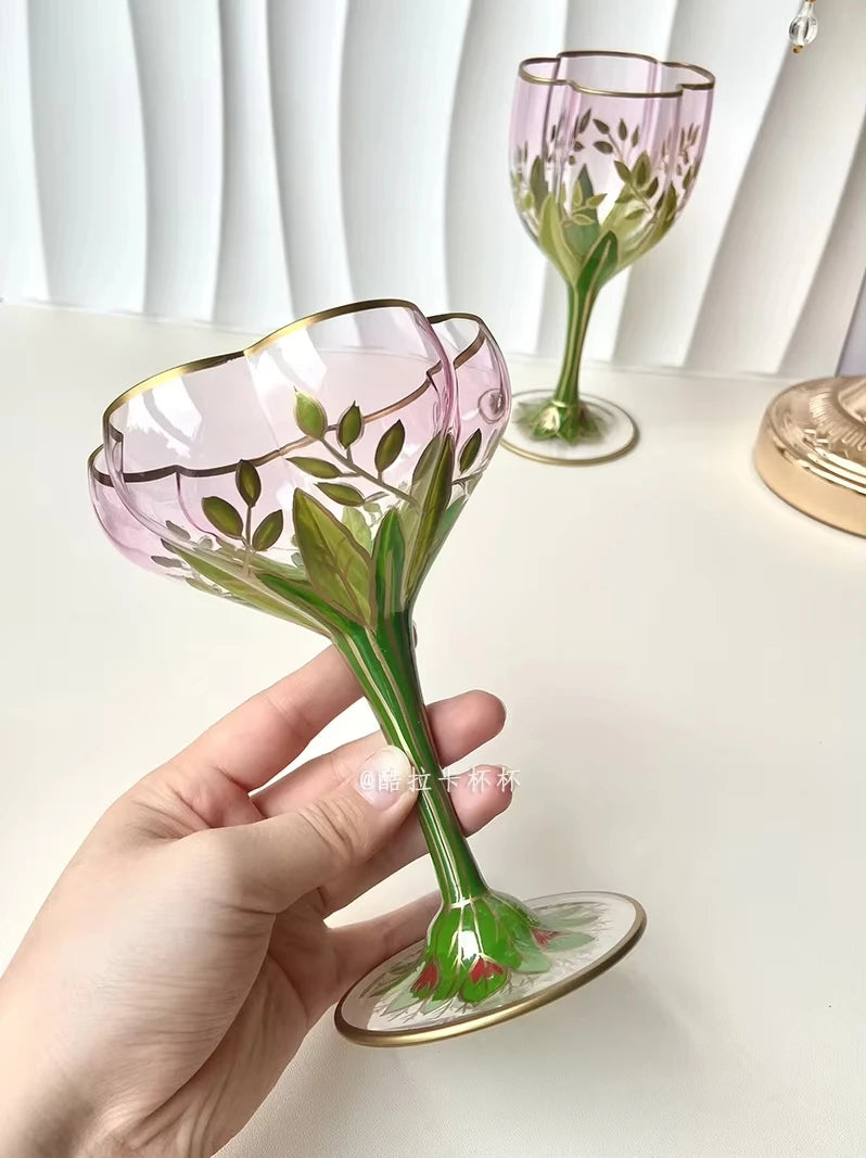 Hand holding a "Botanical Garden" hand-painted crystal martini glass, delicate floral motif detail — CL House Drinkware collection