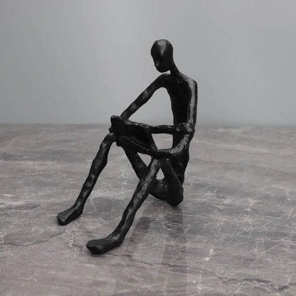 Abstract seated reader sculpture in matte black metal, reading with a book across the knees, on a grey marble surface