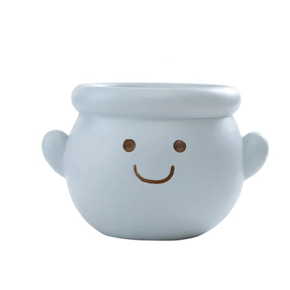 "Happy Pot" smiley face resin succulent planter in sky blue with rounded cauldron shape, side handles and drainage hole, white background