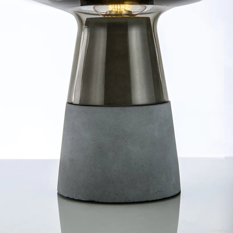  Close-up of the raw cement base and smoked glass stem of the "Smoke & Cement" table lamp with visible filament bulb