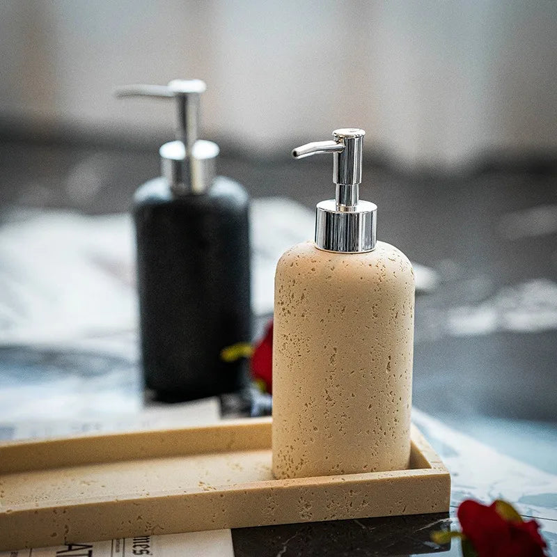 : Rose Stone travertine soap dispenser on wooden tray in foreground with Midnight Stone dispenser blurred behind, styled vignette with red rose detail on dark marble surface