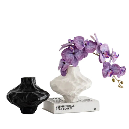  Cloud Form White ceramic vase with purple orchid stems and Black vase beside Design Hotels book, white background