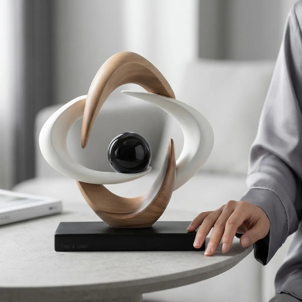 White and gold abstract resin sculpture with a glossy black sphere on a black base, displayed on a round table beside a seated person.