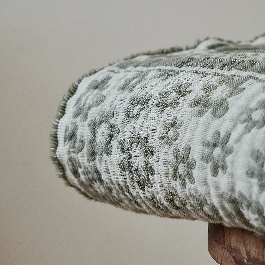 Close-up of rolled Sage Bloom 100% cotton jacquard woven throw blanket showing intricate floral weave texture and overlock edge detail