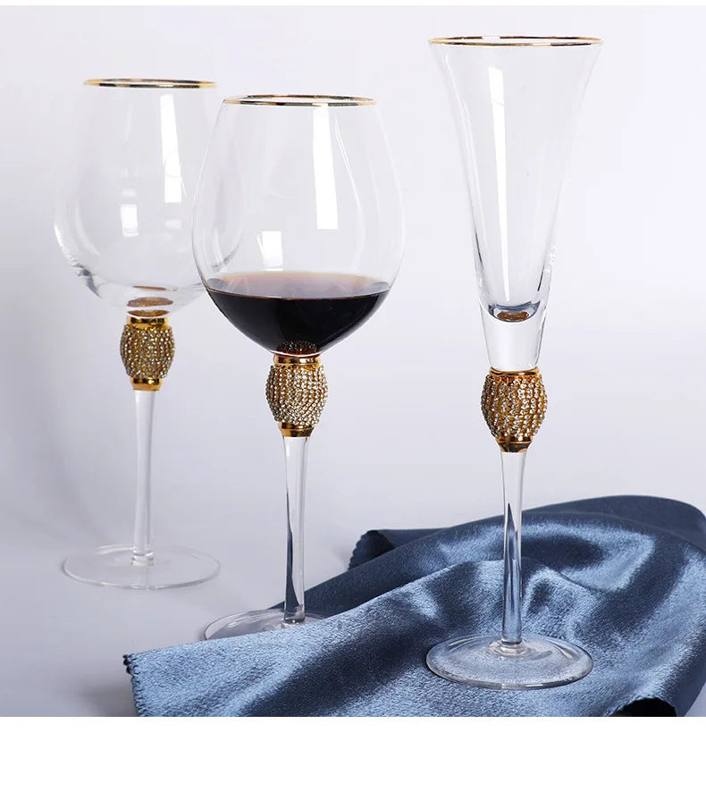"Golden Jewel" Champagne Flute and Wine Glass with micro-crystal bead stems, laid on a draped steel blue satin cloth on a white surface