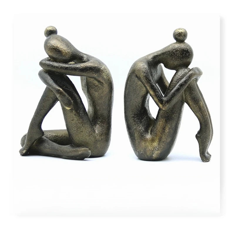 Pair of dark resin abstract seated figures with rounded heads and relaxed poses, displayed side by side against a white background.