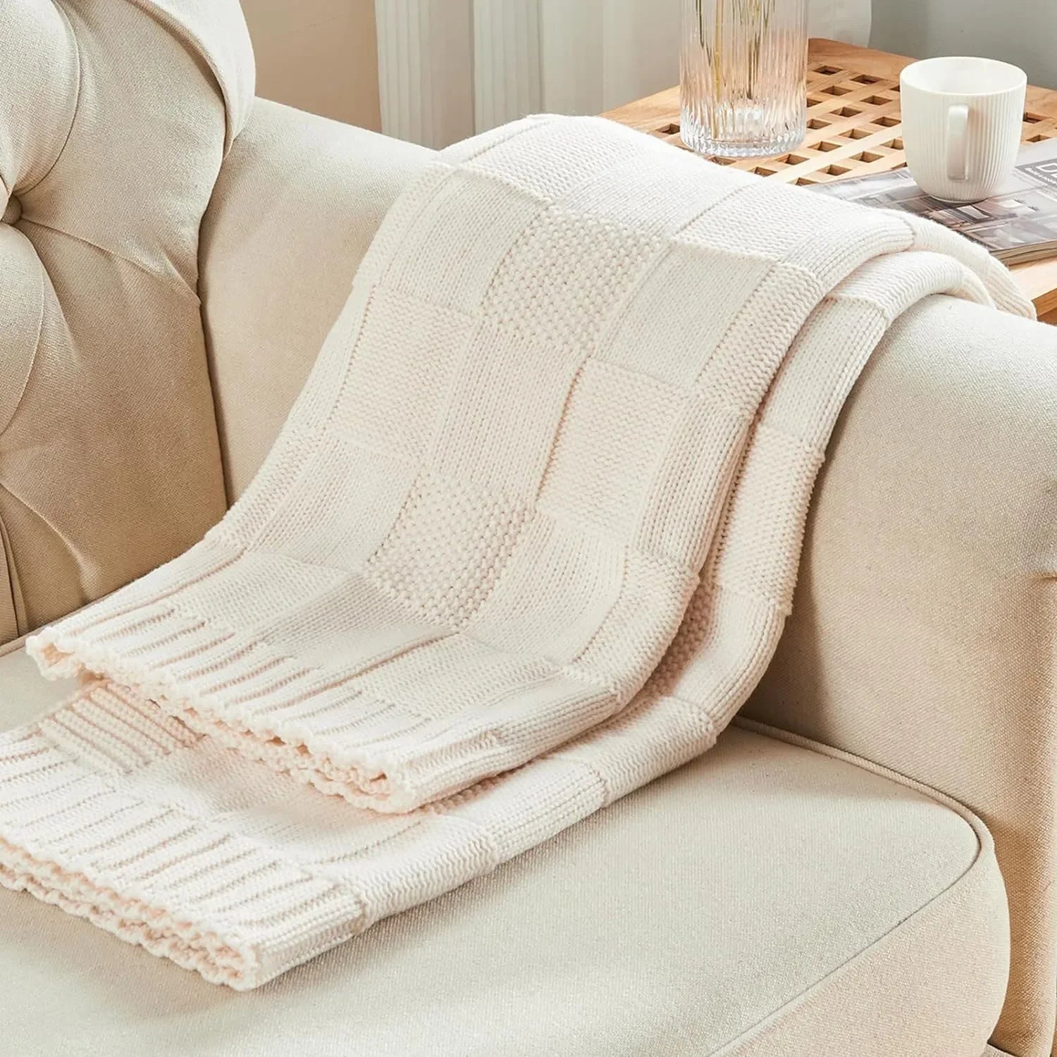 Ivory Cream chunky patchwork knit throw blanket casually draped over a beige tufted sofa — close-up showing the mixed knit texture and ribbed border detail