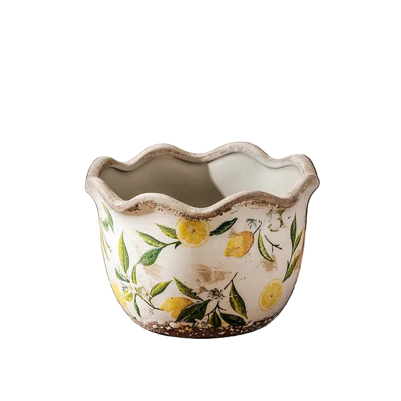 "Lemon Grove" hand-painted ceramic plant pot in Medium size, white crackle glaze with yellow lemon and green leaf print, wavy scalloped rim, shown empty on a rustic wooden surface