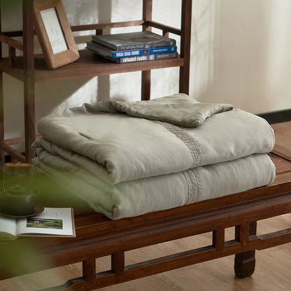Slate grey quilted linen cotton summer throw blanket, neatly folded on a dark wood bench in a japandi-style interior with wooden shelving and open book