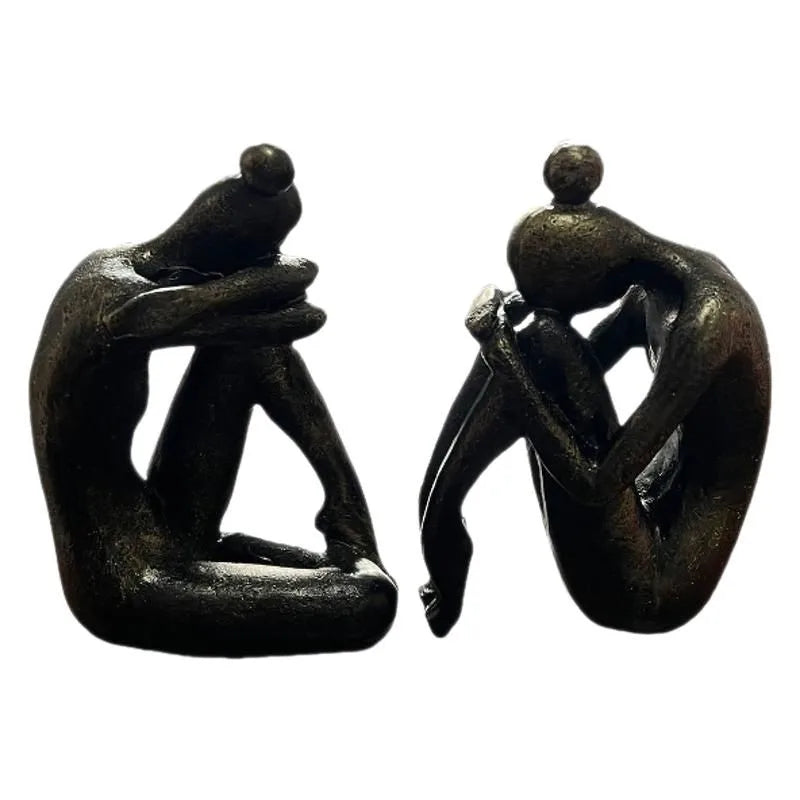 Pair of dark resin abstract seated human figures in different poses, displayed side by side against a white background.