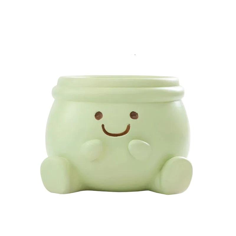 "Happy Pot" smiley face resin succulent planter in sage green with sitting figure design and drainage hole, white background