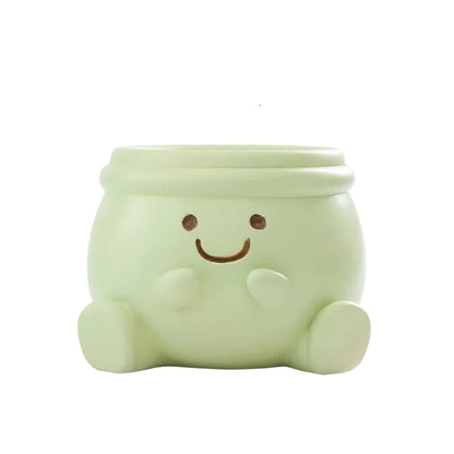 "Happy Pot" smiley face resin succulent planter in sage green with sitting figure design and drainage hole, white background
