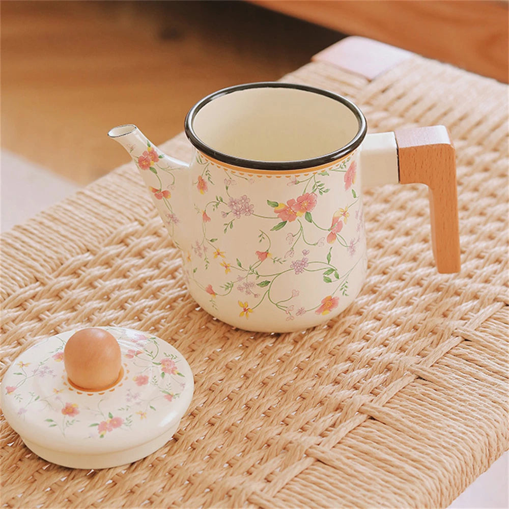 Floral enamel teapot open without lid, showing cream interior and dark rim, with lid placed separately on woven rattan surface — Blossom Kettle by CL House