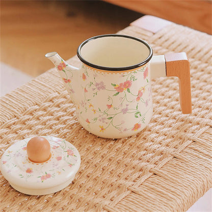 Floral enamel teapot open without lid, showing cream interior and dark rim, with lid placed separately on woven rattan surface — Blossom Kettle by CL House