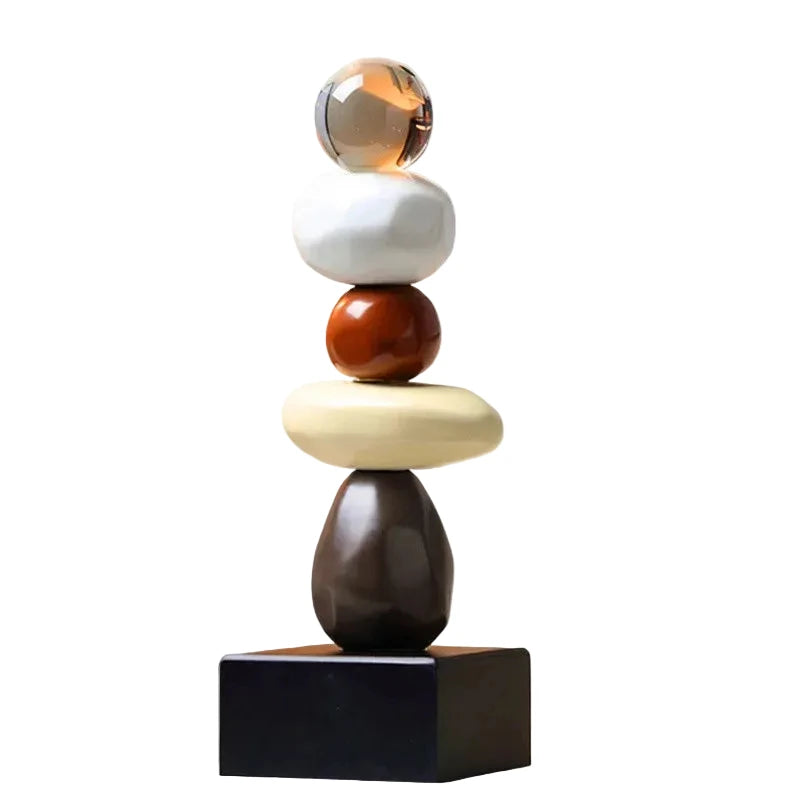 Abstract ceramic stacked sculpture with a clear upper sphere, white and brown rounded forms, a cream oval element and a black square base, displayed against a white background.