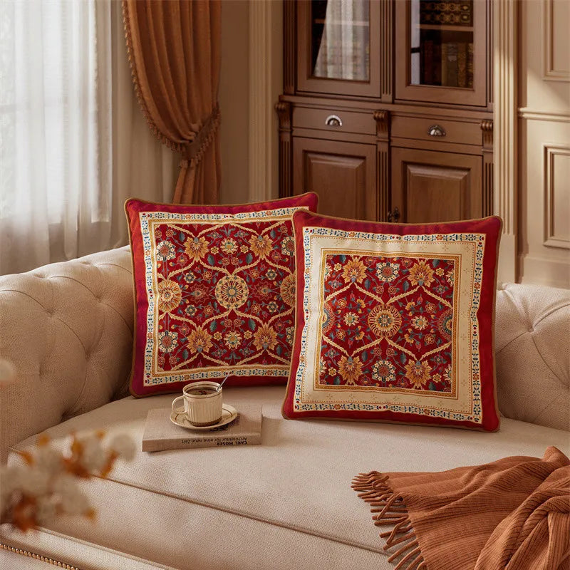 "Crimson Court" Persian velvet cushion cover styled on a cream tufted sofa — two sizes shown side by side, deep crimson ground with amber and teal medallion floral pattern, gold piping detail — CL House