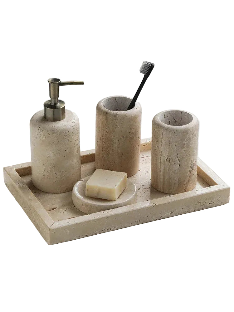 Natural travertine bathroom accessory set on white background — soap dispenser with bronze pump, toothbrush cup, mouthwash cup, soap dish and rectangular tray in warm beige stone — wabi-sabi bathroom decor