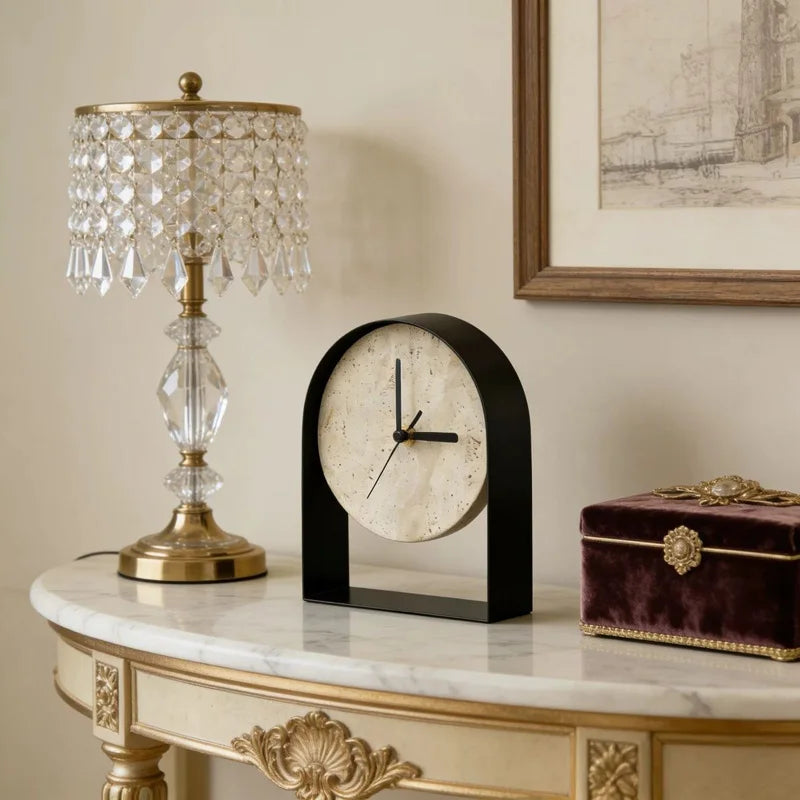 Alt text:

Black arched travertine table clock styled on a marble console table beside a crystal lamp and a velvet jewellery box