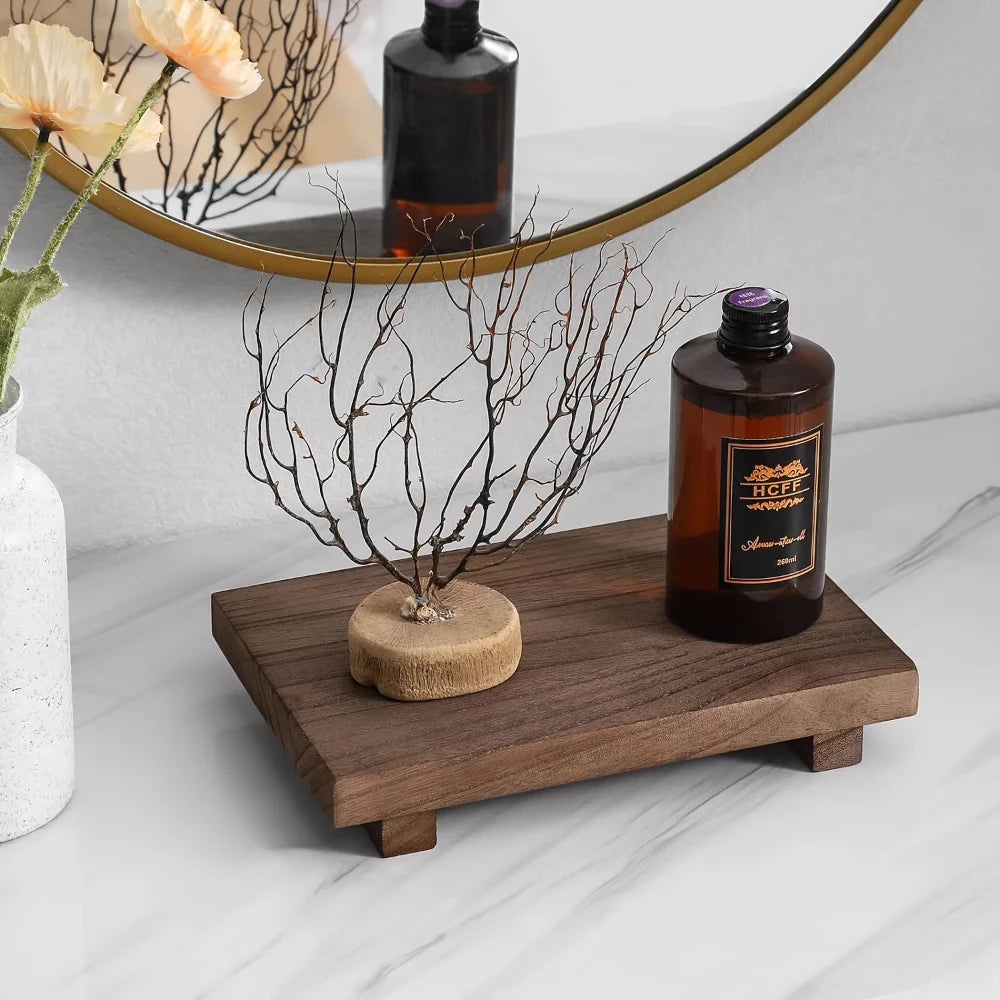 Walnut wood elevated bathroom tray on marble surface styled with dried branch sculpture and amber glass bottle, gold round mirror in background — wabi-sabi bathroom decor