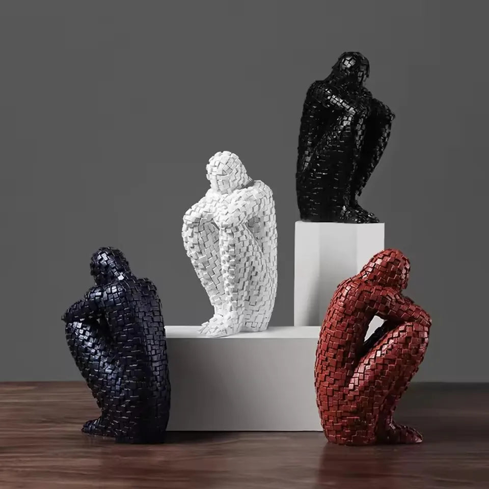 Four mosaic resin figure sculptures in white, black and red finishes arranged on white blocks and a wooden table.⠋