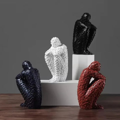 Four mosaic resin figure sculptures in white, black and red finishes arranged on white blocks and a wooden table.⠋