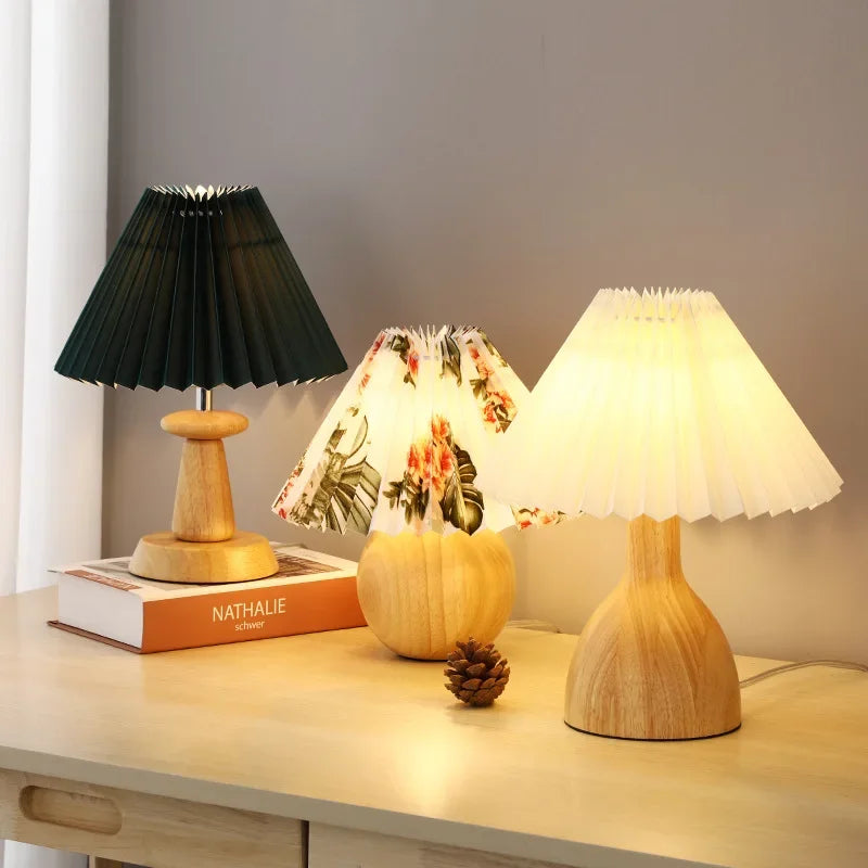  Three "Pleat & Wood" pleated table lamps displayed together — forest green, floral, and off white shades with spool, sphere, and vase wood bases on a sideboard