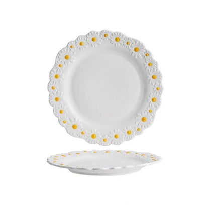 "Daisy Bloom" ceramic dinner plate — top and profile view on white background showing raised daisy relief border with white petals and golden yellow centres, soft white glaze and scalloped edge — product shot