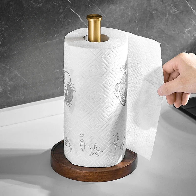 Alt text para a foto 6:

Hand pulling a sheet from a kitchen paper roll on the Walnut & Gold Paper Towel Holder — walnut wood base and gold rod on a white countertop, dark marble wall background.
